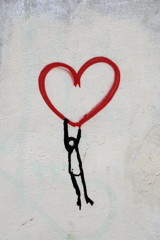stick-figure-hanging-from-a-red-heart-shape-pointed-on-wall
