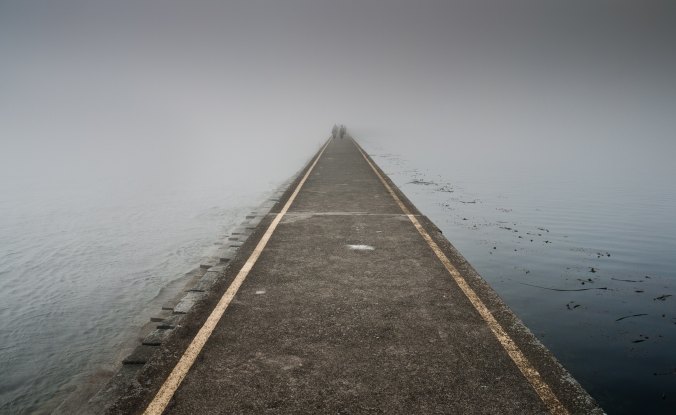 pathway through misty gray lake with two figures in the distance